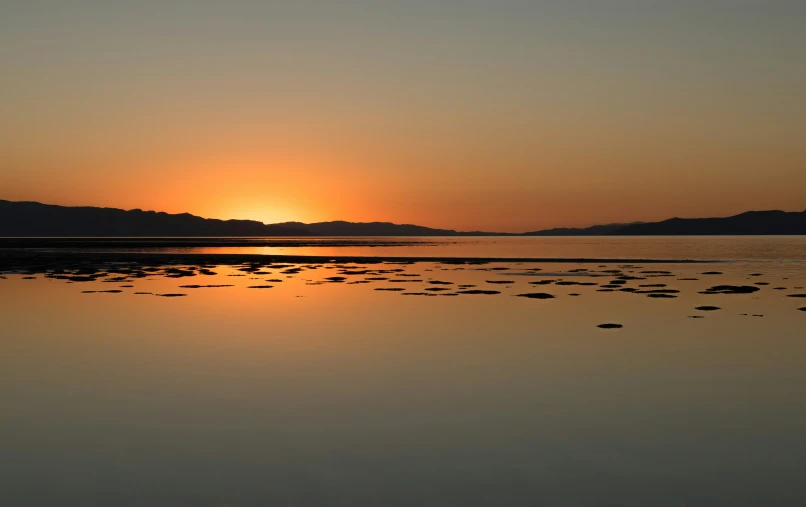 a sunset over some low hills and a body of water