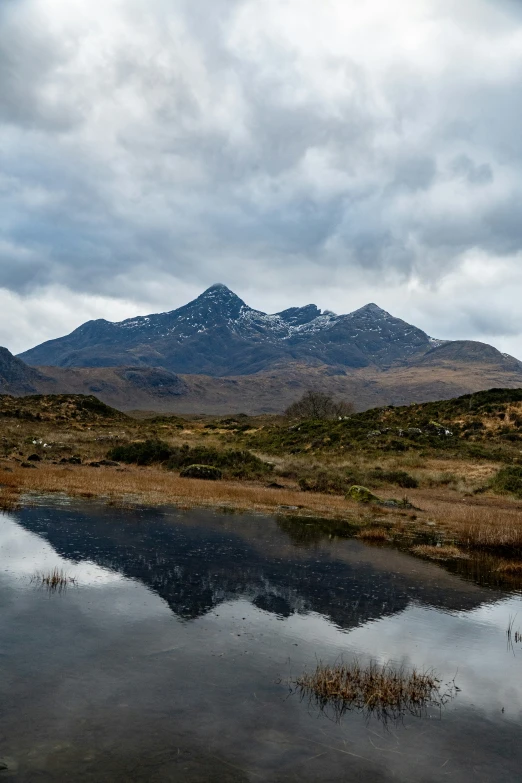 the landscape shows the water, grass, and mountains with a reflection in the lake