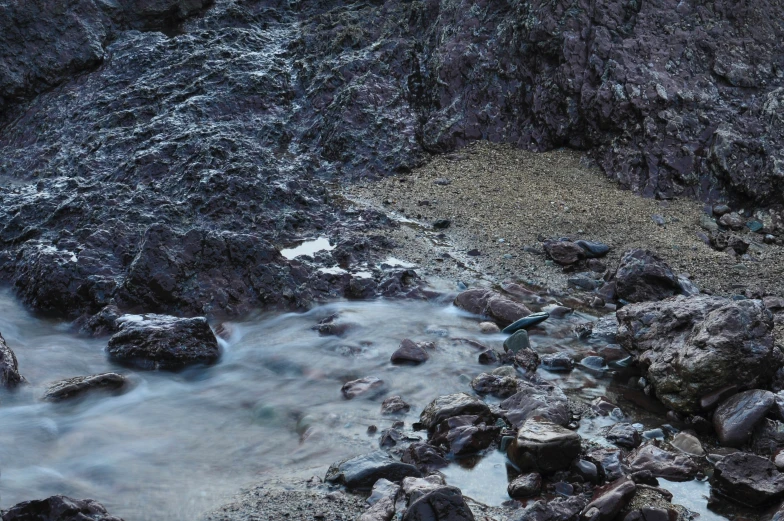 water is rushing over rocks on a sandy beach