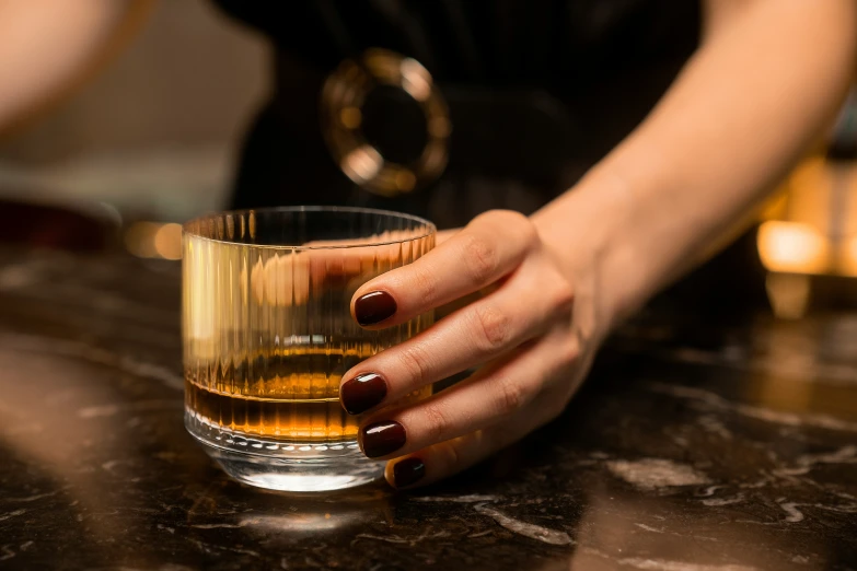 someone holding a glass of whiskey while sitting at a table