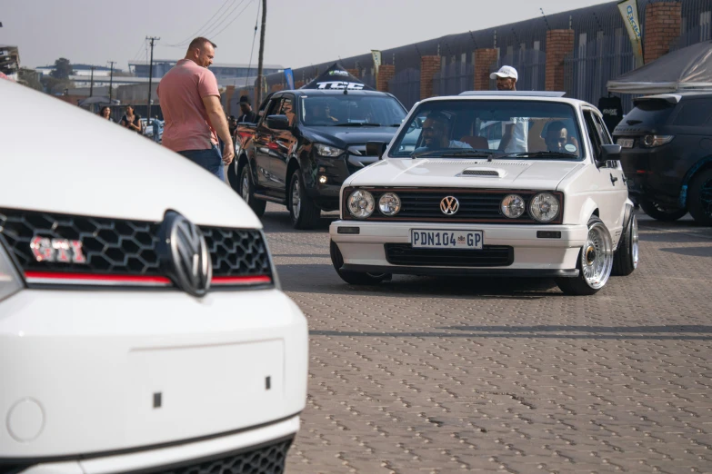 two white cars traveling down the road while people stand by