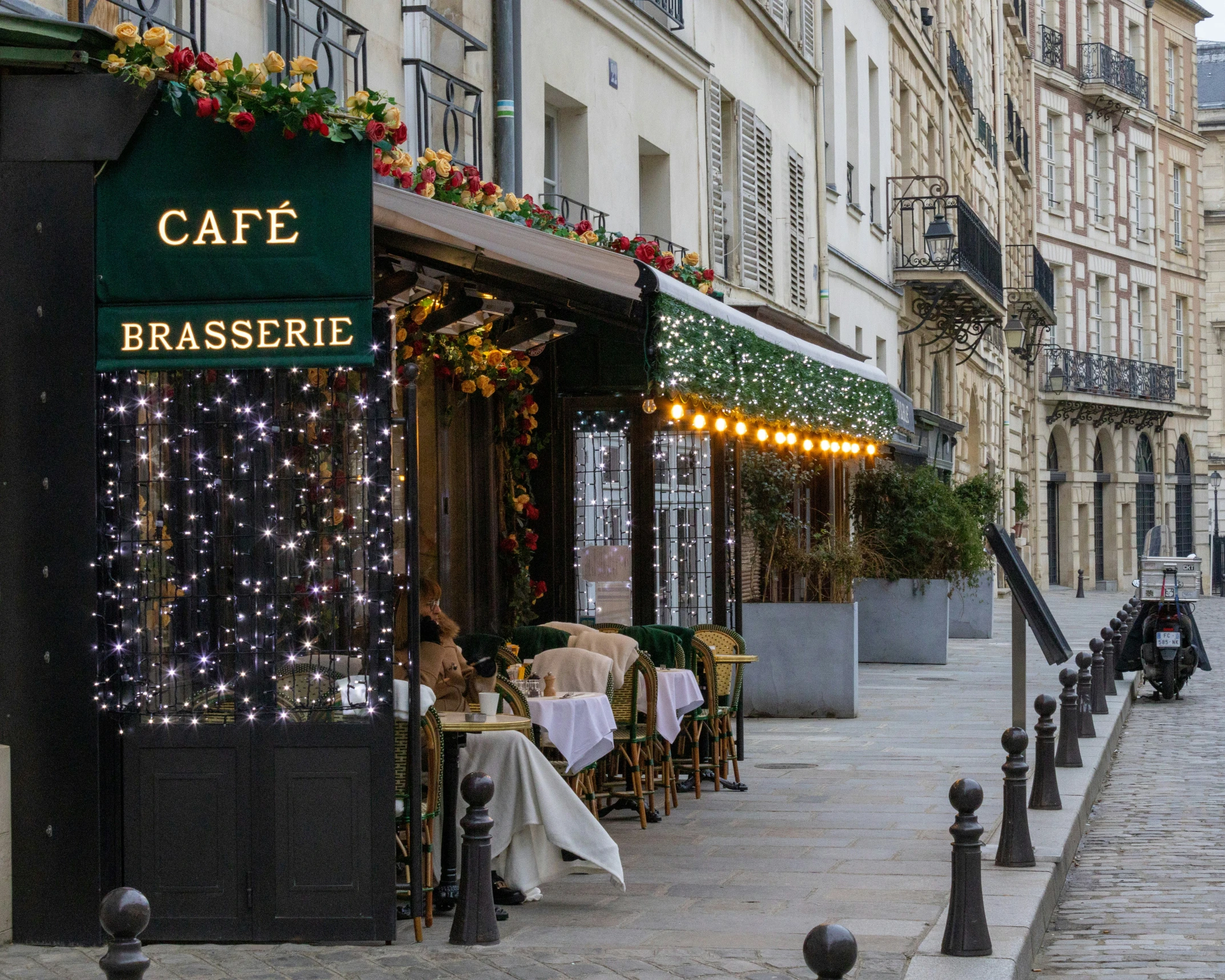 a woman is outside of the cafe with a long white table cloth and lights on it