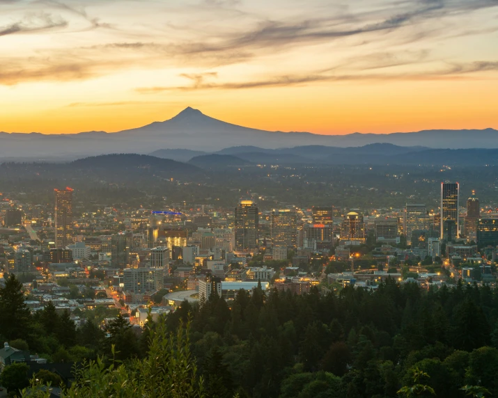 a cityscape at sunset with tall buildings and mountain range in background