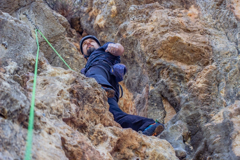 a man in jeans and a jacket climbing up the side of a rock face