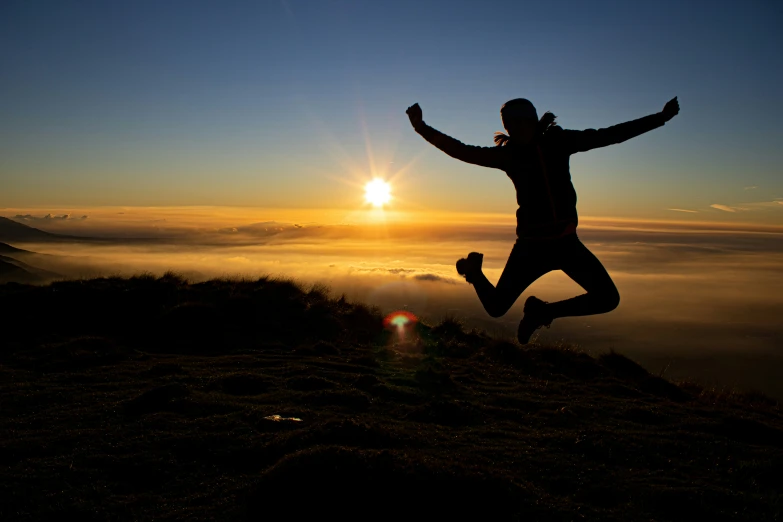 the silhouette of a person leaping in the air on top of a hill