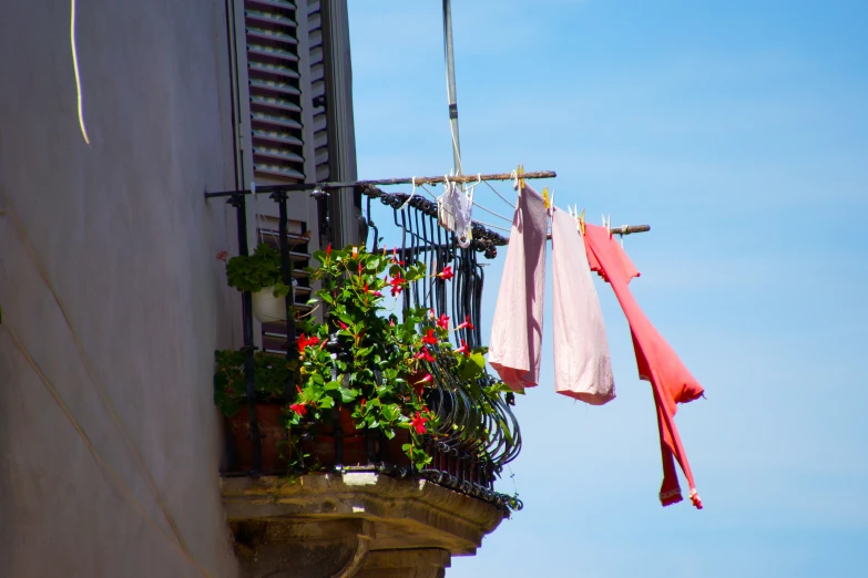 clothes are hanging on a balcony with pots and potted plants