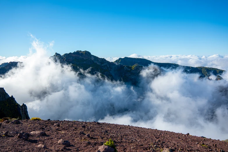 clouds covering mountains below a blue sky