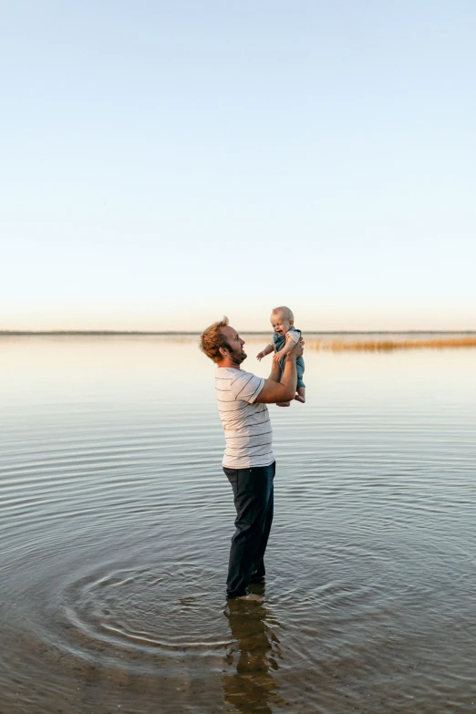 an adult holding a baby on his shoulders while in the water