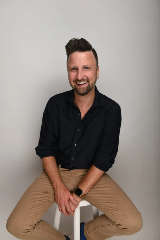 a smiling man poses with his legs crossed
