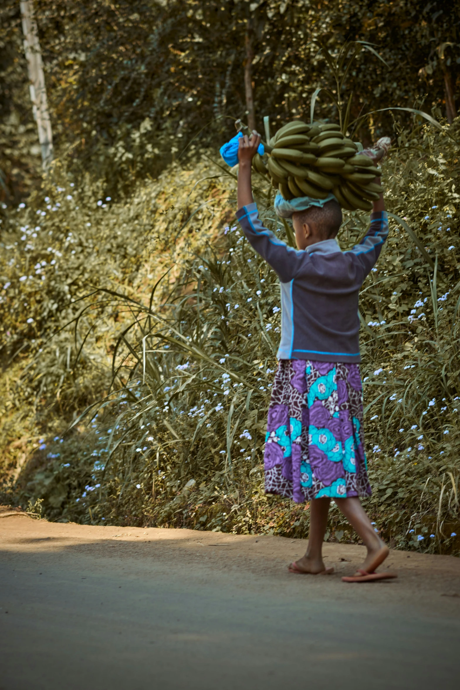 a child carrying a lot of ripe green bananas