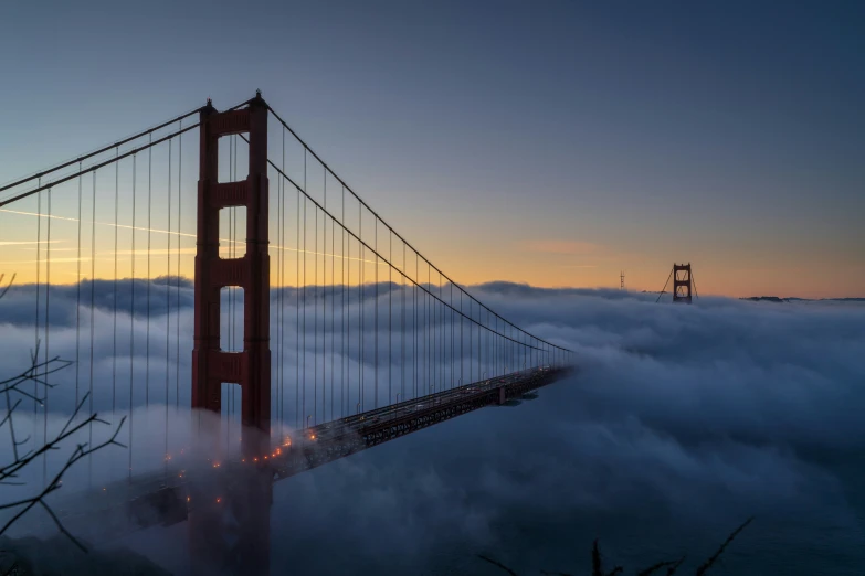 a fog filled valley of water and a suspension bridge at sunrise