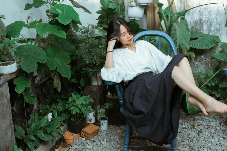 a woman in white shirt sitting in blue chair next to plants