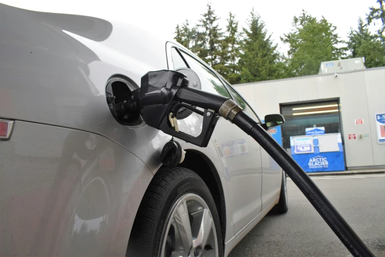 the front of a silver car at a gas station filling up