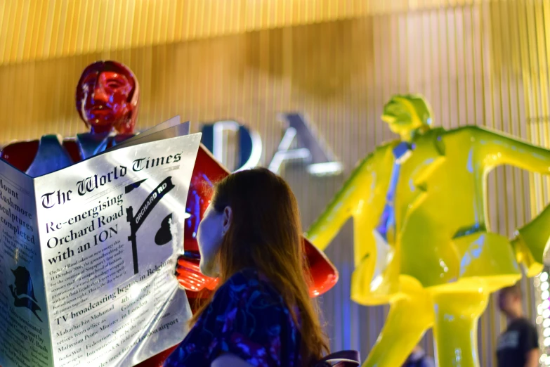 a woman reads a paper next to a statue of an iron man