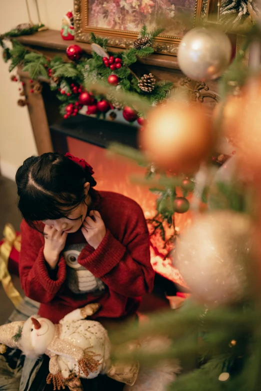 a woman sits next to a decorated tree talking on the phone