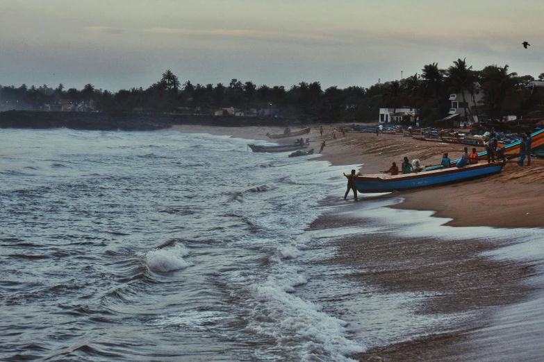 some people are standing on the beach by boats