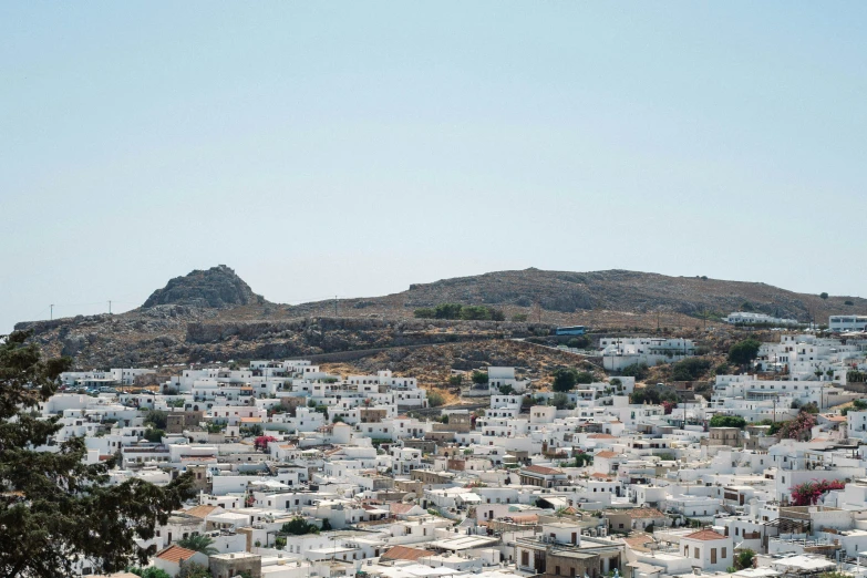 a hillside with several small white buildings on the bottom and mountains behind it