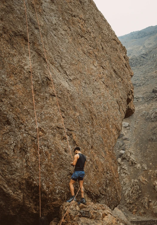 man climbing up the side of a mountain near a rope