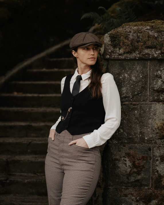 woman in a suit, hat and tie leaning on a wall