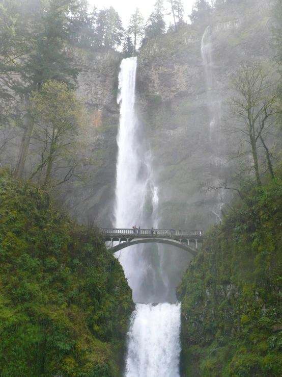 an arched waterfall and a bridge in the fog