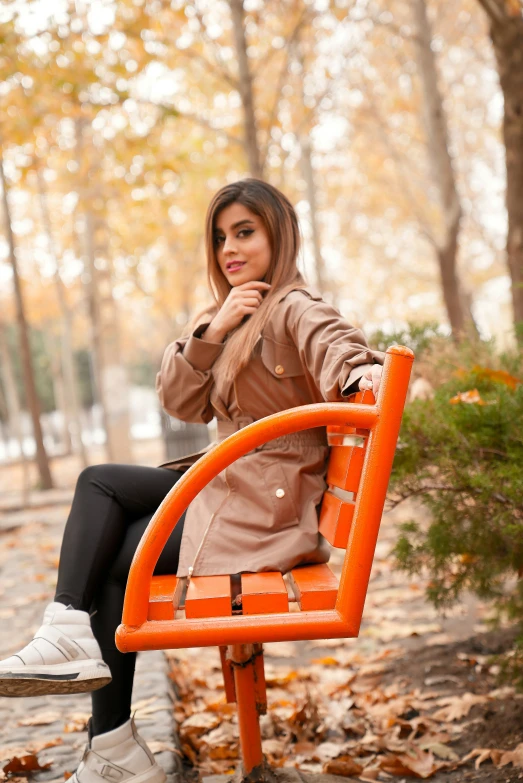 a woman is sitting on an orange chair in the middle of a tree lined park