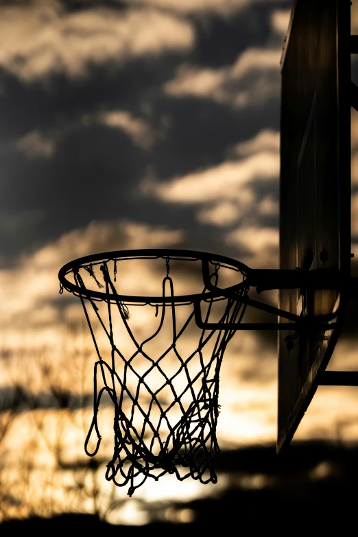 the silhouette of a basketball hoop and a cloudy sky