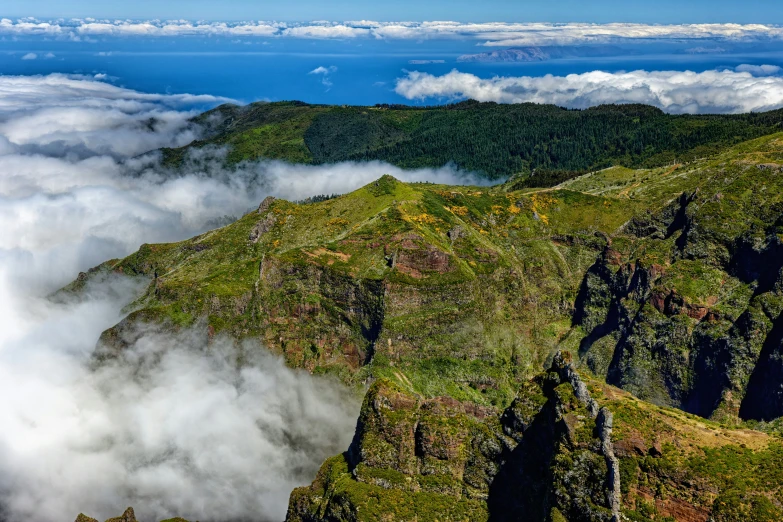 a view of the top of a mountain with clouds flying over it