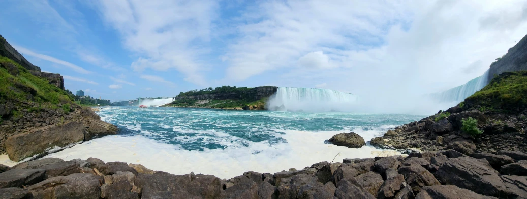 a waterfall next to the rocky shore under a blue sky