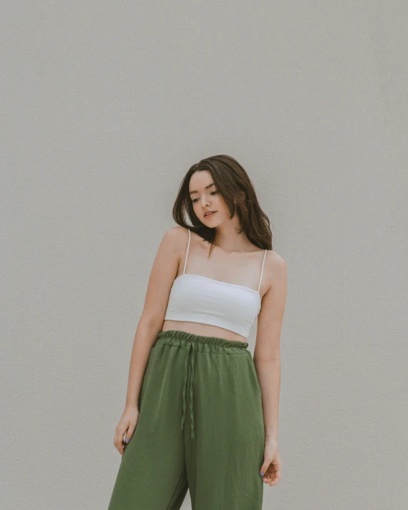 a woman standing against a wall wearing green pants