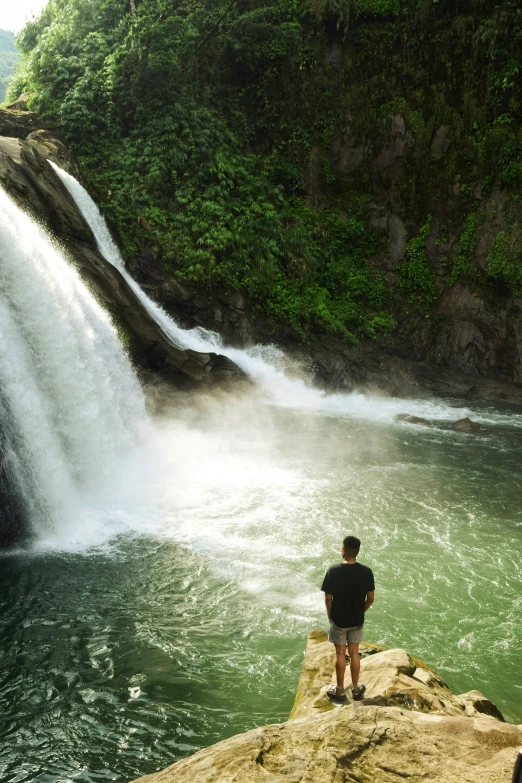 the man is standing on the cliff below the water fall