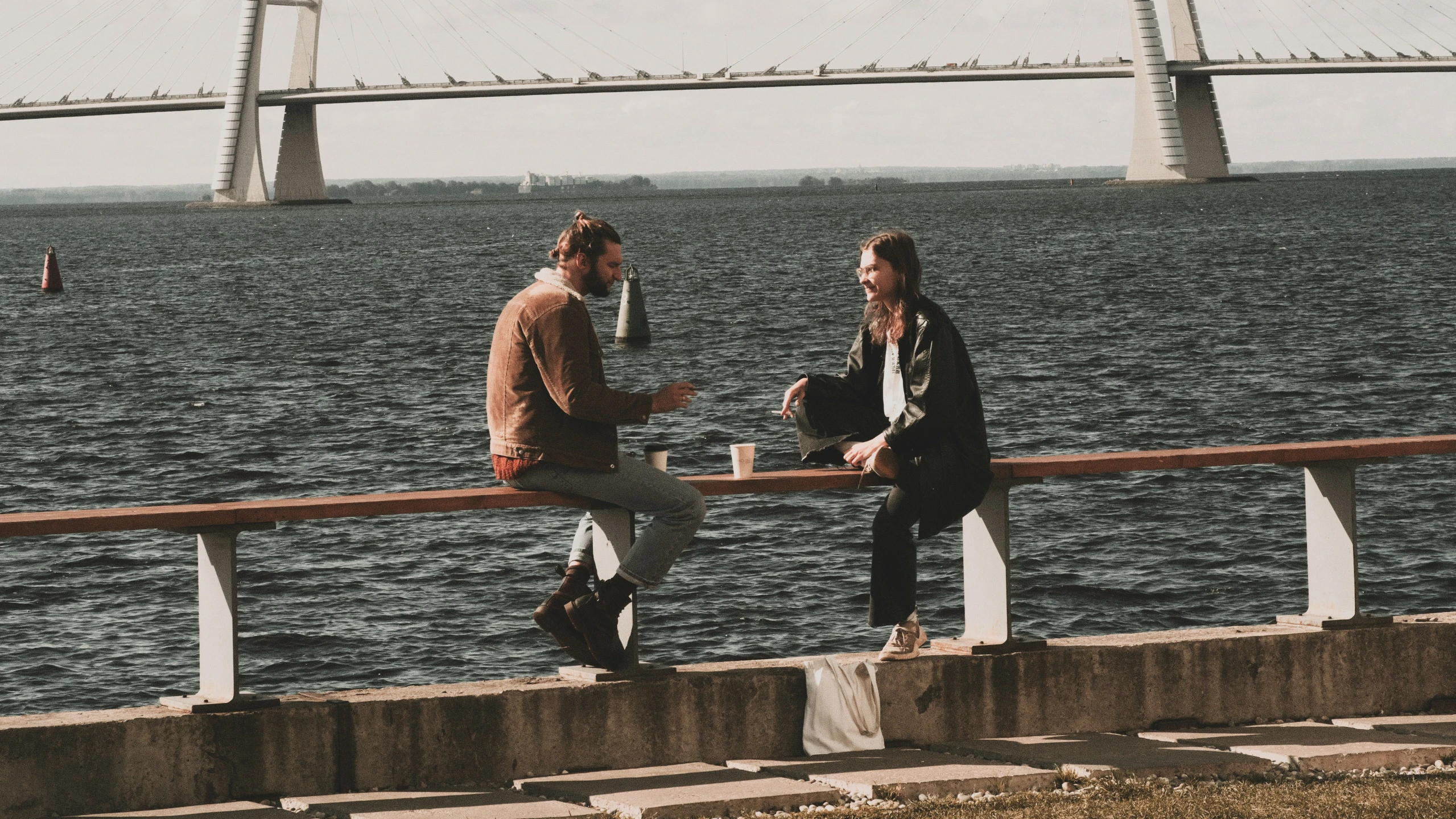 two men standing next to each other on the side of a bridge