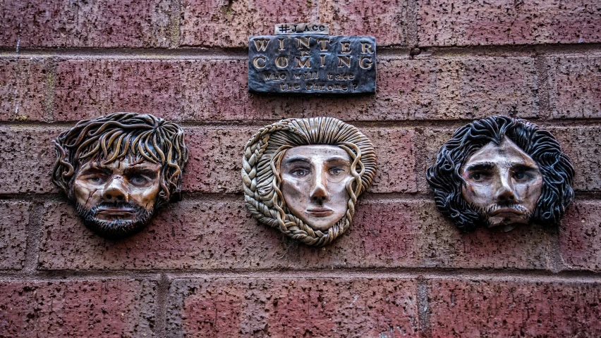 three faces on a brick wall, two painted in plaster and one with a roped off wire attached to it
