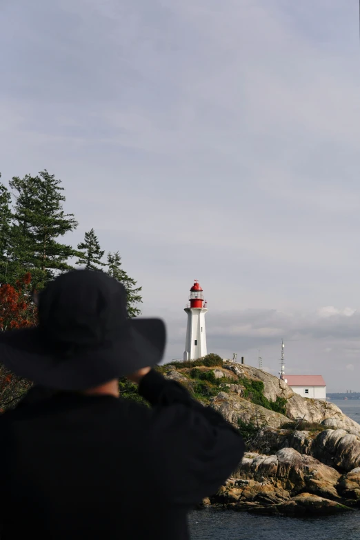 person in black jacket facing lighthouse from rocky cliff