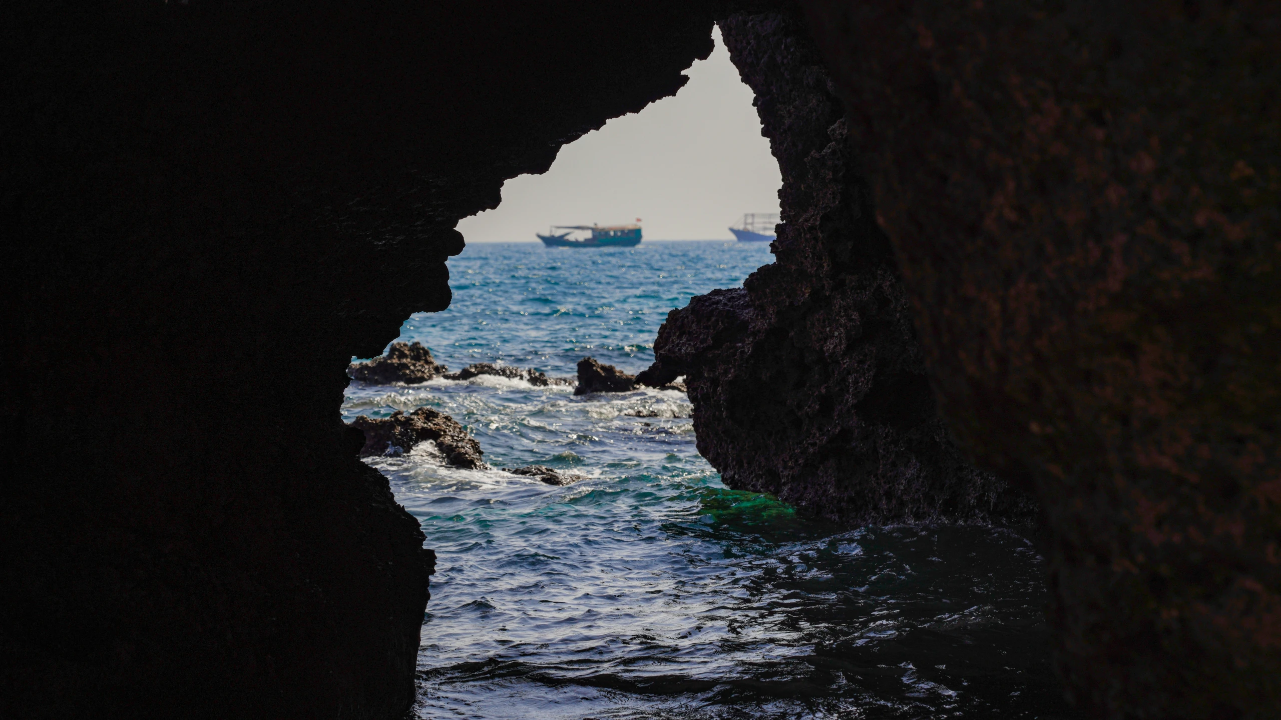 a boat is going across the ocean while a cave in the rocks is opened