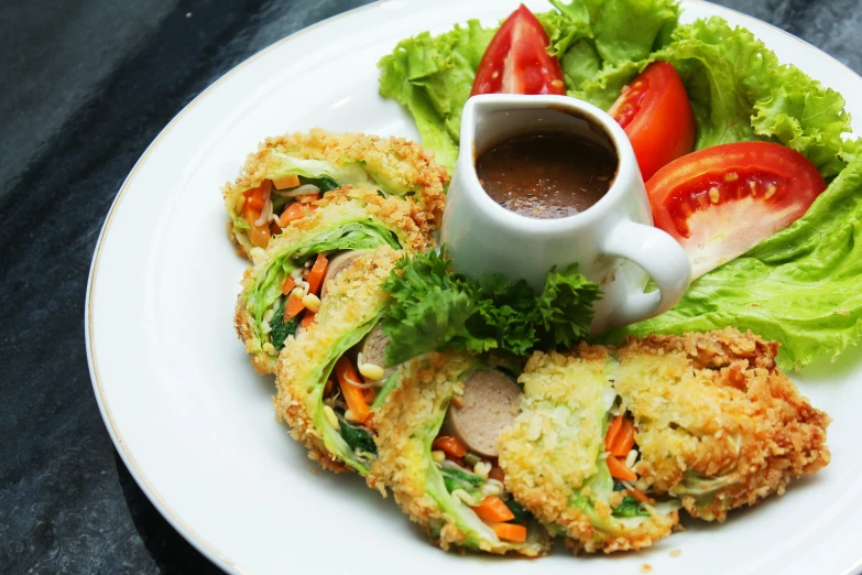 fried food with sauce served on plate with greens and tomatoes