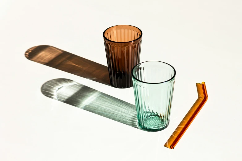 three different colored glass cups and an orange straw