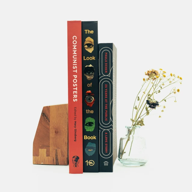 three books on the same bookcase and one on each of them with a vase of flowers in front of the book