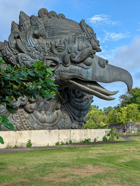 there is a dragon statue made up of wood and surrounded by lush green trees