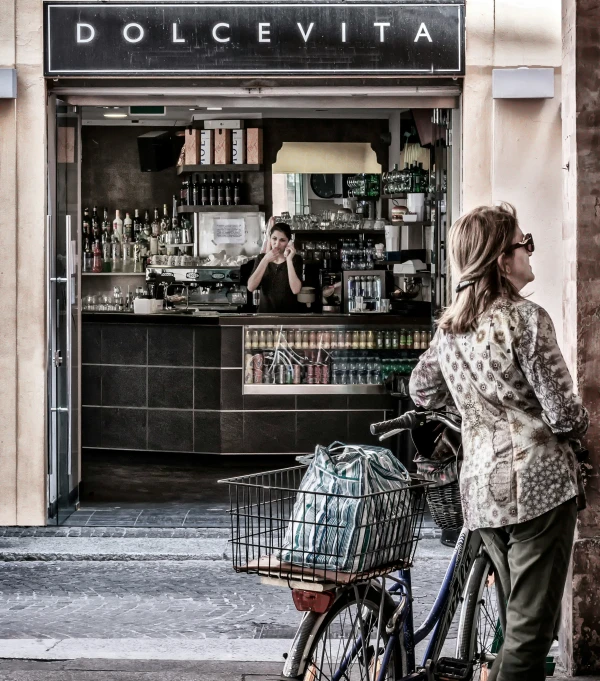 a woman stands outside of an italian shop with her bicycle