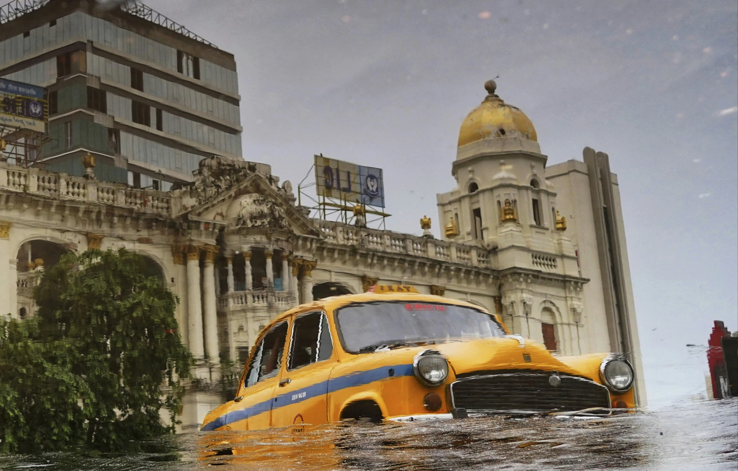 a yellow taxi drives through water in front of buildings