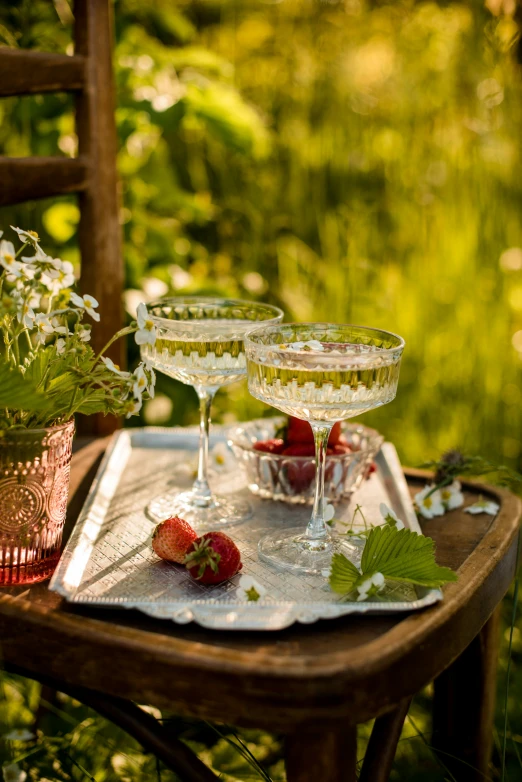 two glasses of champagne and strawberries sit on a tray on a table outside