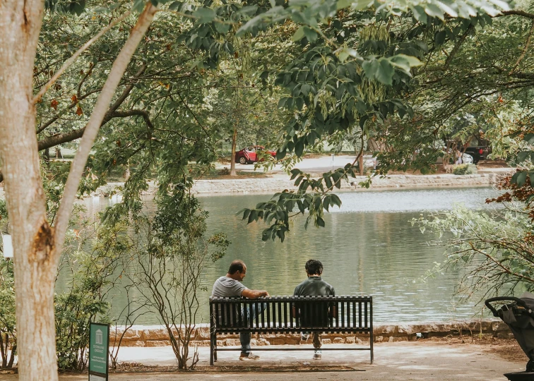 two men sitting on a bench in front of a lake