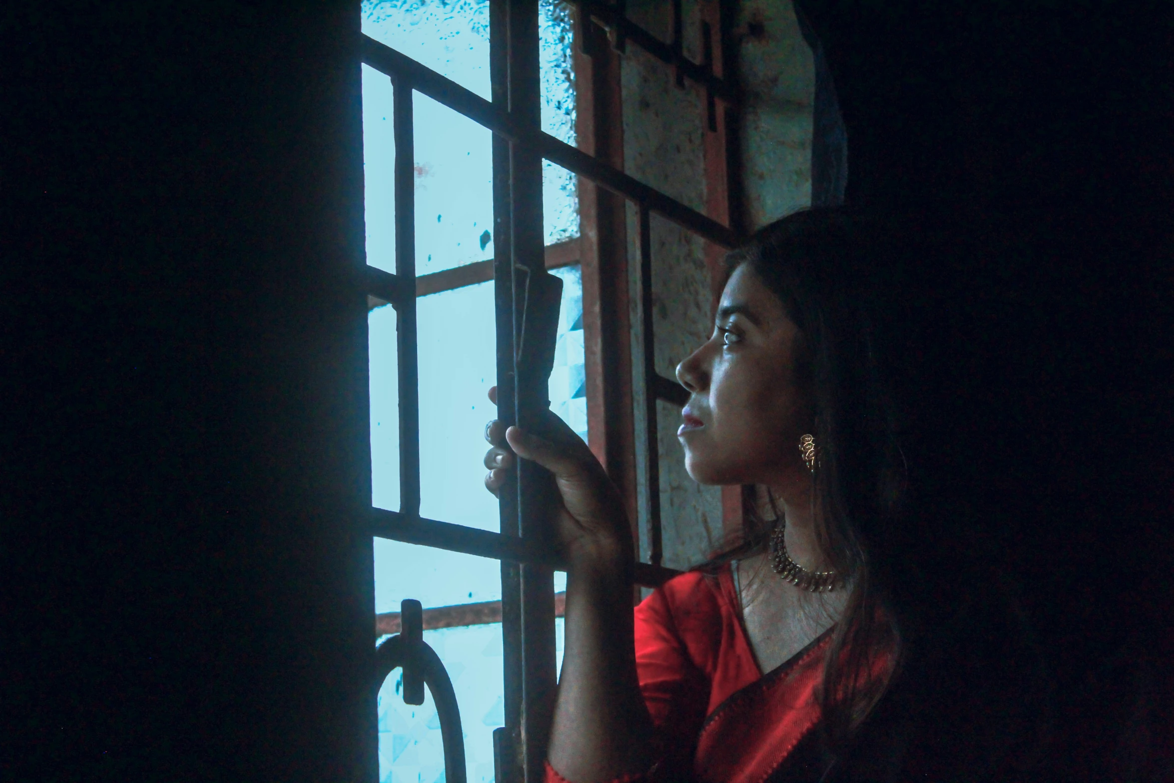 a woman in red standing by a window with black curtain