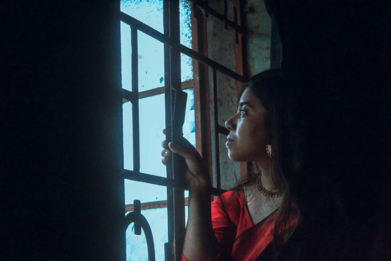 a woman in red standing by a window with black curtain