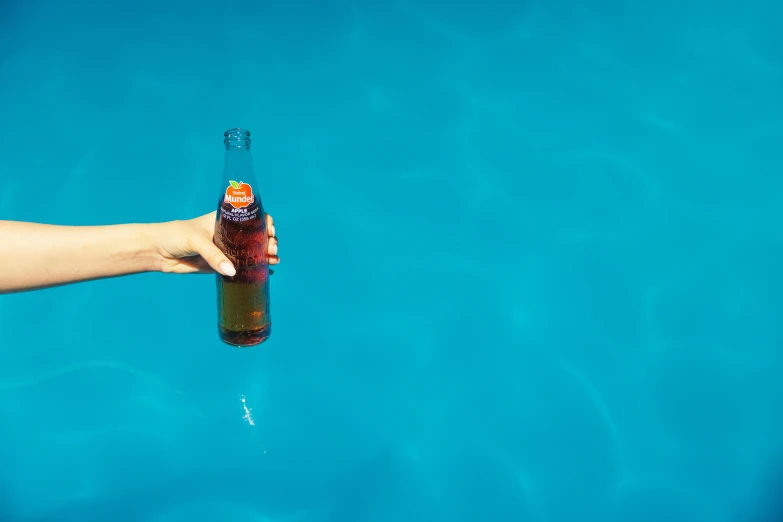 a person holding onto a beer in a swimming pool