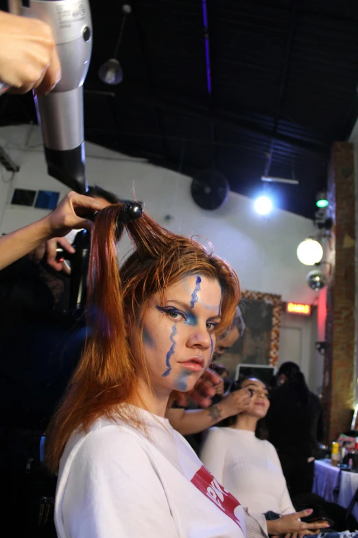 a woman with face paint getting her hair styled