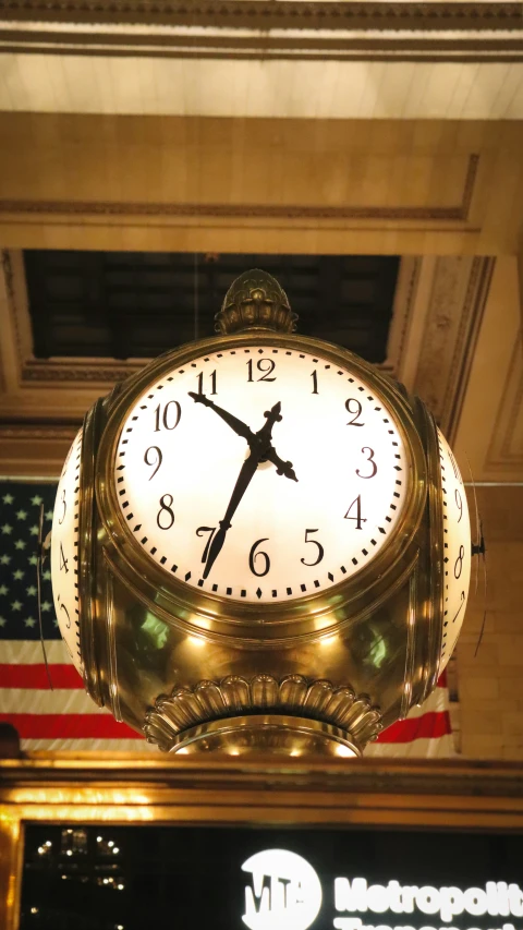 large clock attached to ceiling above american flag