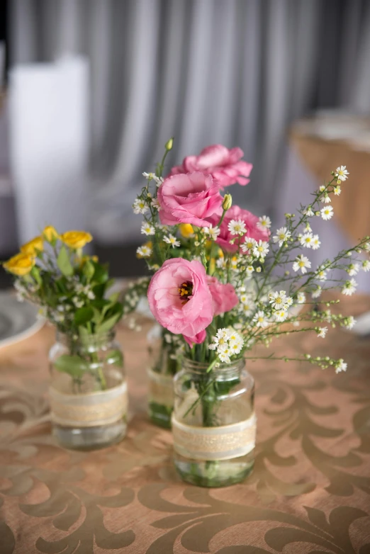 several glass jars on a table hold colorful flowers