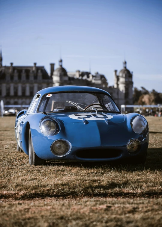 old blue sport car sits in front of an old castle