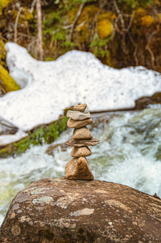 a stack of rocks sits atop a rock in front of a rushing water
